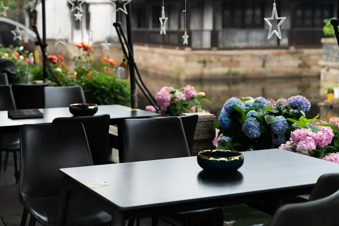 Outdoor cafe tables and chairs beside a canal in Majorca, adorned with potted flowers and hanging star-shaped lights, create a luxury lifestyle atmosphere against the backdrop of charming buildings.