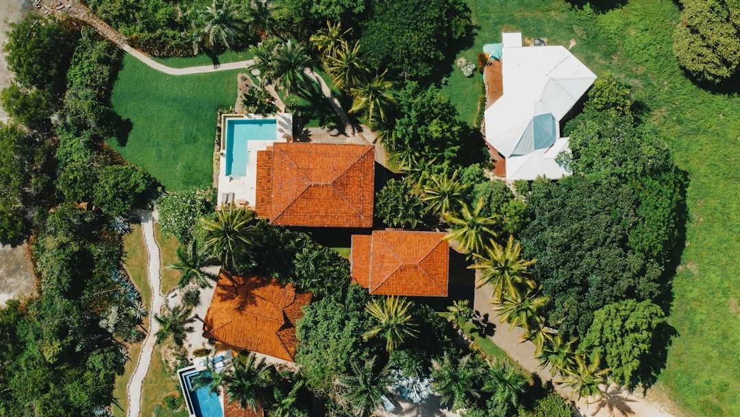 Aerial view of luxury houses with red-tiled roofs and a white roof in Majorca, surrounded by trees and greenery, featuring two swimming pools for an enviable lifestyle.