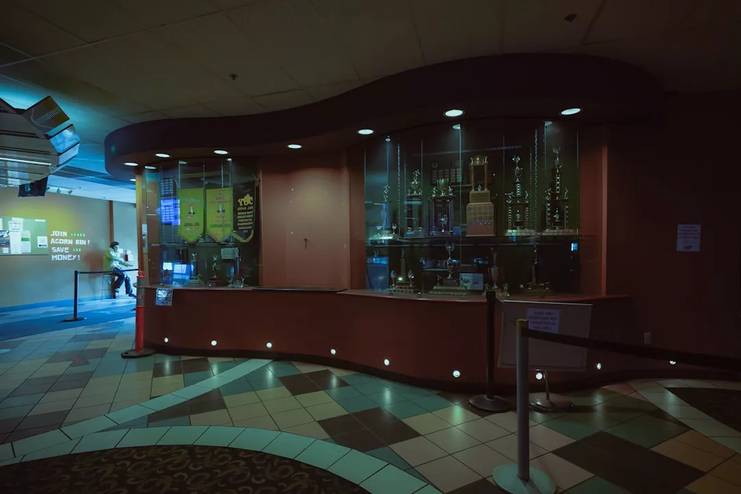 A dimly lit movie theater lobby with a glass trophy case displaying awards, a ticket counter, and tiled flooring exudes a touch of luxury and sophistication.