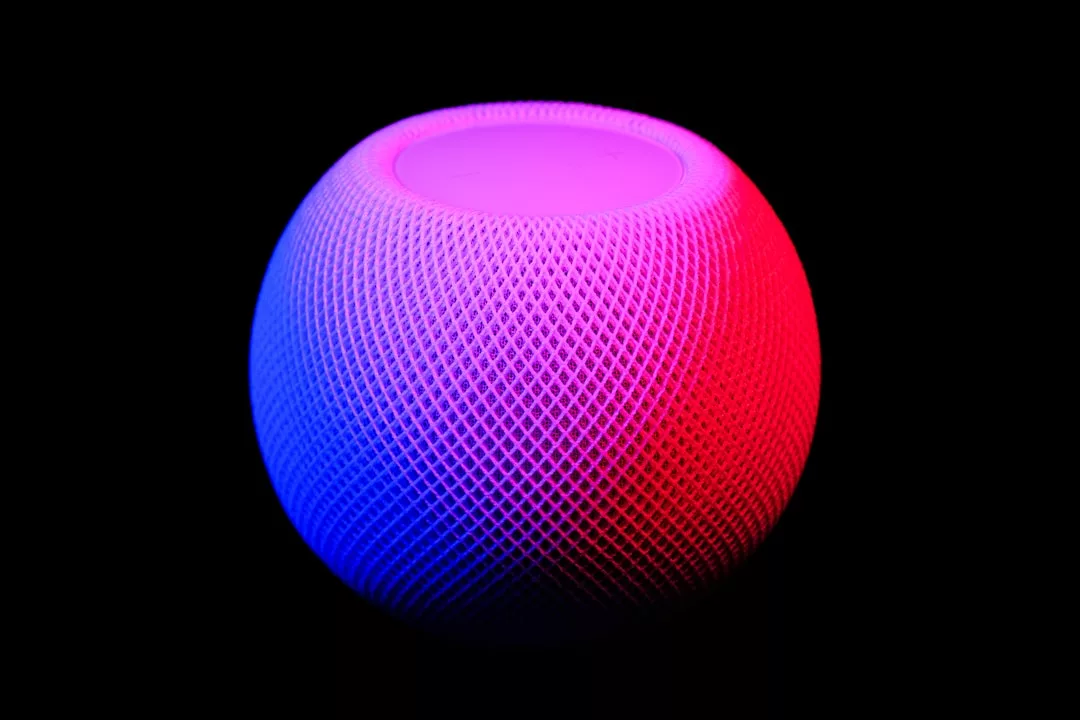 A spherical smart speaker with a mesh surface, illuminated by pink and blue lights, evokes a sense of luxury lifestyle against a sleek black background.