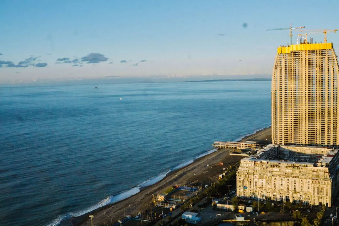 A tall luxury building under construction stands by the coastline of Majorca, with a sandy beach, calm sea, and clear sky in the background—a glimpse into an exclusive lifestyle.