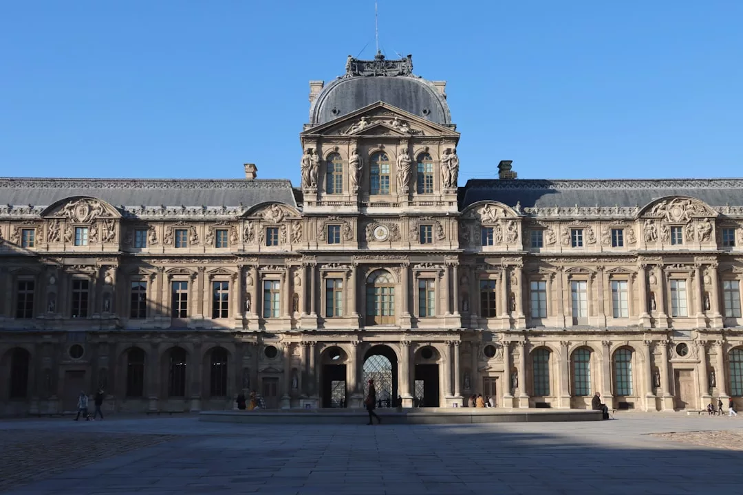 The image shows the historic Louvre Palace in Paris, featuring ornate stone architecture, tall arched windows, and a central domed pavilion under a clear blue sky—evoking timeless luxury reminiscent of a Majorca lifestyle.