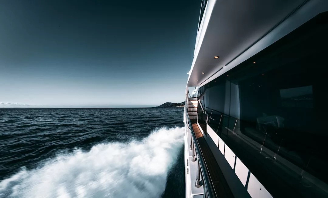 Side view of a luxury yacht moving quickly across calm ocean water near Majorca, with waves forming along the hull and a distant shoreline visible under a clear sky—a scene of pure lifestyle elegance.