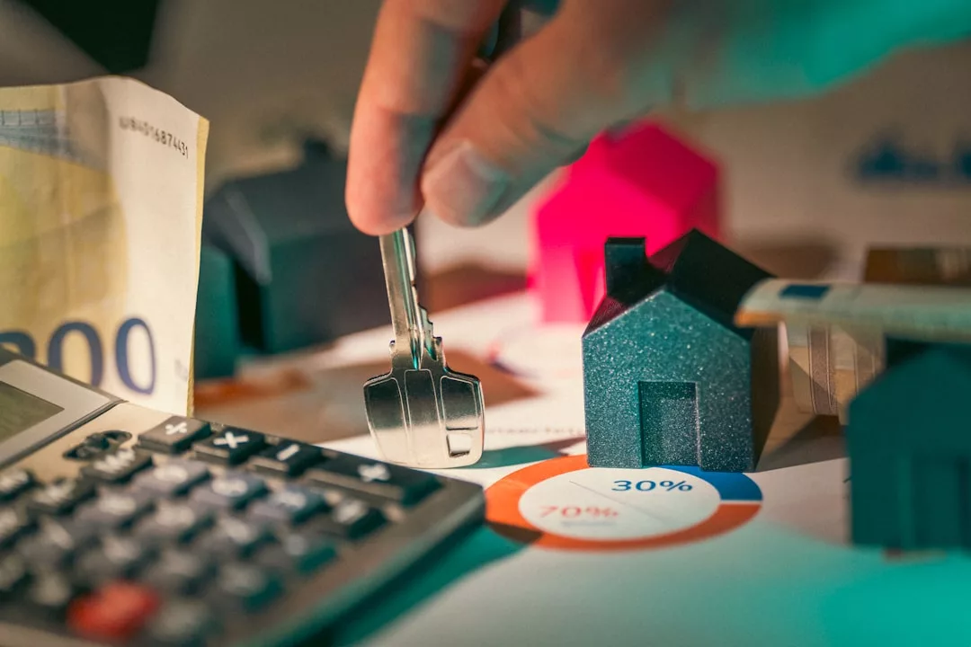 A hand holds house keys above a small model house, with a calculator, euro banknote, and financial charts in the background—capturing the luxury lifestyle of home ownership in Majorca.