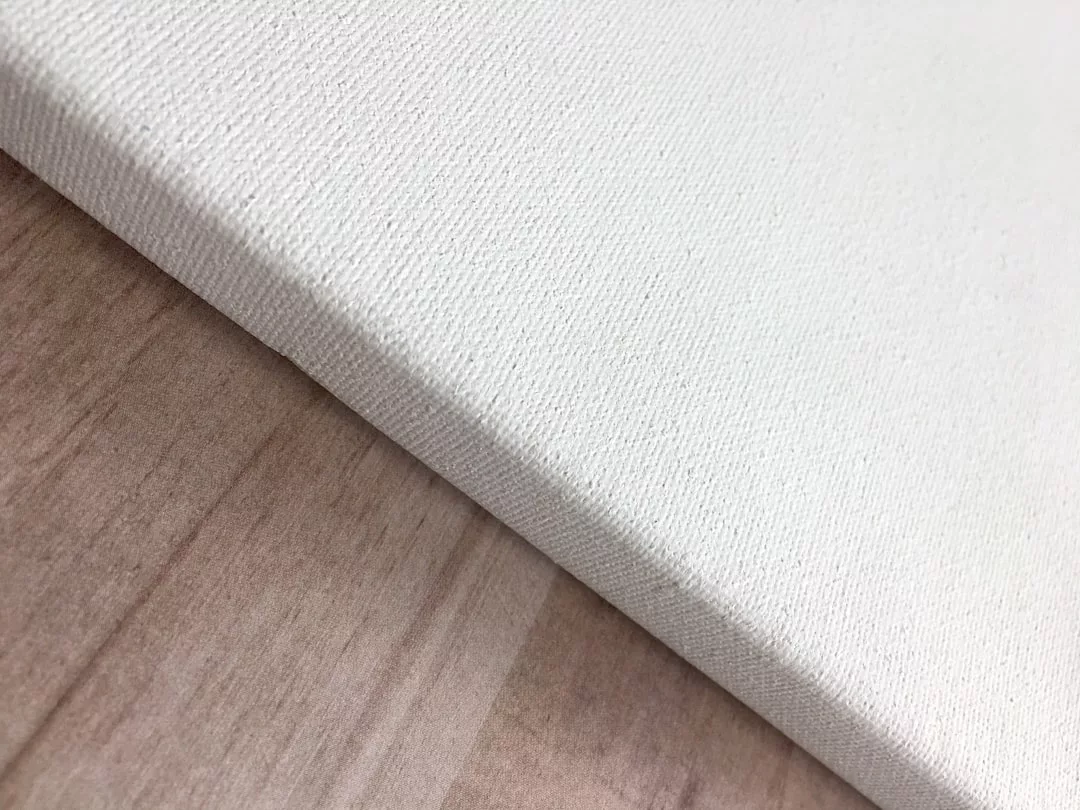 A close-up of a blank white canvas resting on a light wooden surface in a luxury setting, highlighting the canvas texture and edge.