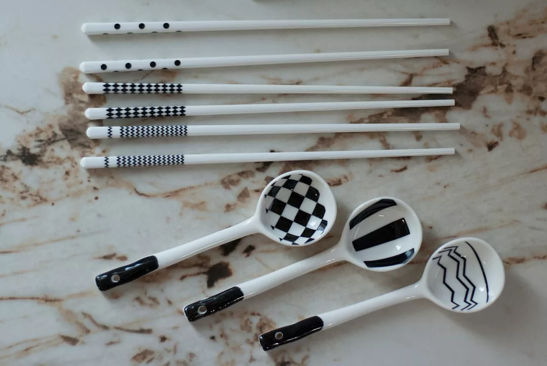 Four white ceramic spoons and six pairs of white chopsticks with various black geometric patterns, arranged neatly on a marble surface, add a touch of luxury to your dining lifestyle.