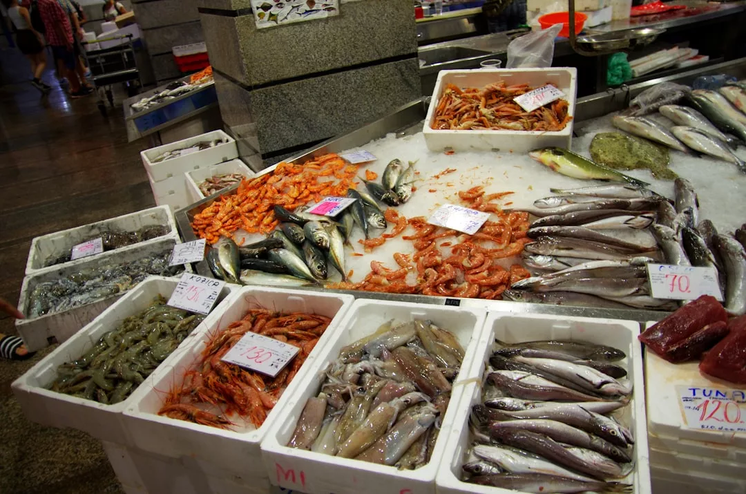 Fresh seafood display at a Majorca market featuring various fish, shrimp, and squid laid on ice in white styrofoam boxes—perfect for those seeking a taste of local luxury lifestyle.