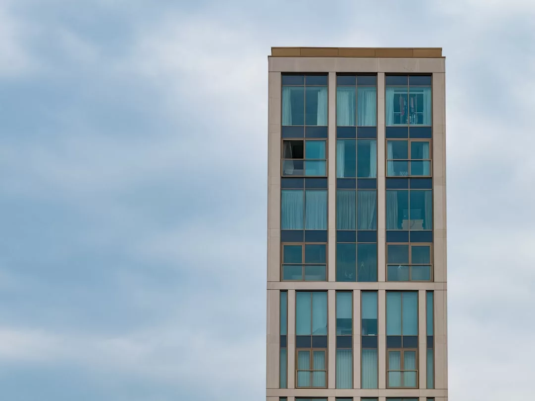 A modern high-rise building with large blue-tinted windows stands against a cloudy sky, offering a glimpse of luxury lifestyle inspired by Majorca.