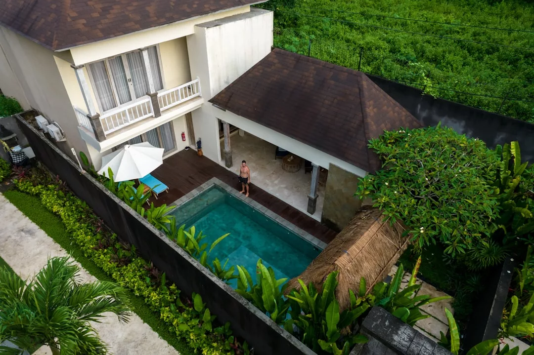 A person stands by a small private pool next to a two-story villa with a patio and tropical landscaping, enjoying the luxury lifestyle of Majorca, all viewed from above.