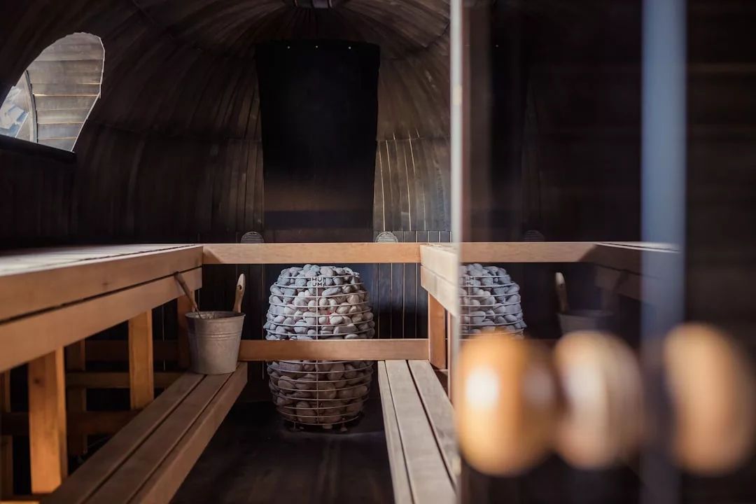 Luxury wooden sauna interior with benches on both sides, a bucket with ladle on the left bench, and two metal baskets filled with sauna stones in the center—perfect for an elevated lifestyle experience inspired by Majorca.