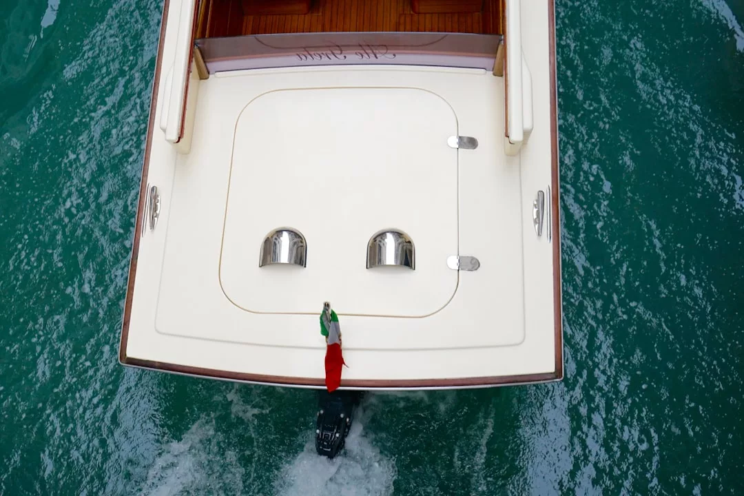 Aerial view of the stern of a white luxury yacht with two vents, a small Italian flag, and a motor, floating on greenish-blue water—perfect for embracing the lifestyle of Majorca.