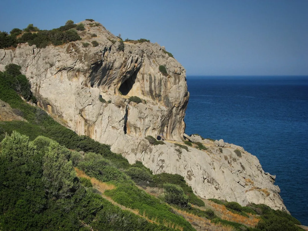 A large rocky cliff with sparse vegetation rises above the blue sea under a clear sky, capturing the luxury lifestyle vibe of Majorca’s stunning coastline.