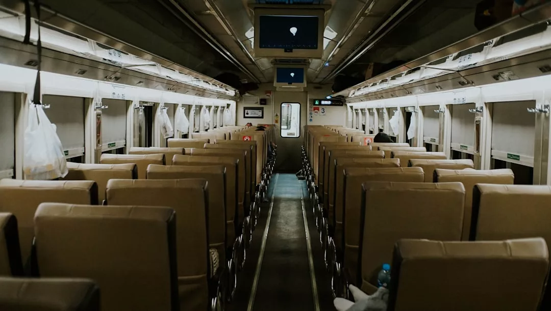 Experience a glimpse of daily lifestyle in Majorca with this interior view of an empty train carriage, featuring rows of brown seats, overhead luggage racks, plastic bags hanging, and a screen at the front.