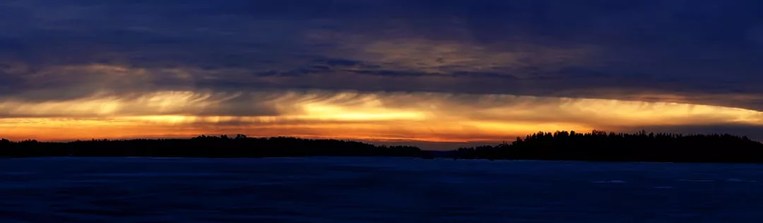 A dark silhouette of land and trees is visible beneath a dramatic, golden sunset sky with layered clouds over the waters of Majorca, capturing the essence of luxury lifestyle amid breathtaking natural beauty.
