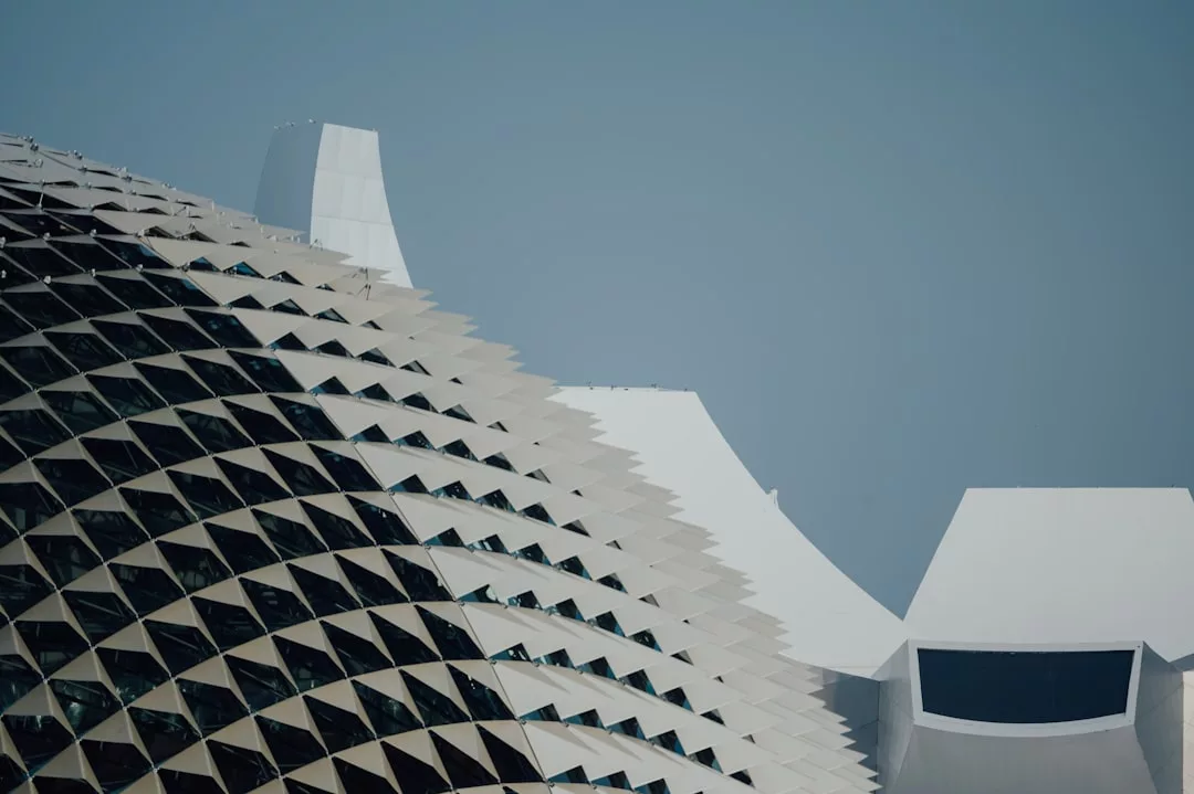 Close-up view of a modern Majorca building facade with geometric, triangular panels and white, angular roof structures in the background, evoking a sense of luxury under a clear sky.