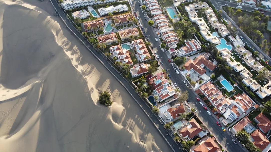 Aerial view showing a sharp boundary between a luxury residential neighborhood with pools and the vast sandy desert area, capturing the unique lifestyle reminiscent of Majorca’s exclusive retreats.