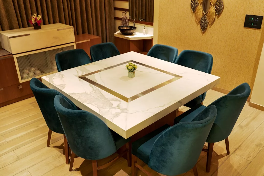 A square marble dining table with a small plant centerpiece, surrounded by eight blue velvet chairs, adds a touch of luxury to this modern dining room—perfect for elevating your lifestyle in Majorca.