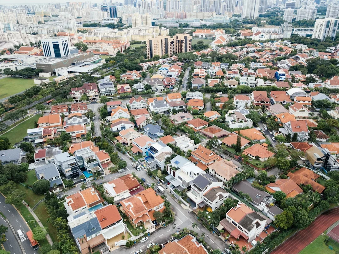 Aerial view of a luxury residential neighborhood in Majorca, with rows of houses featuring red and grey roofs, tree-lined streets, and several high-rise buildings in the background offering an upscale lifestyle.