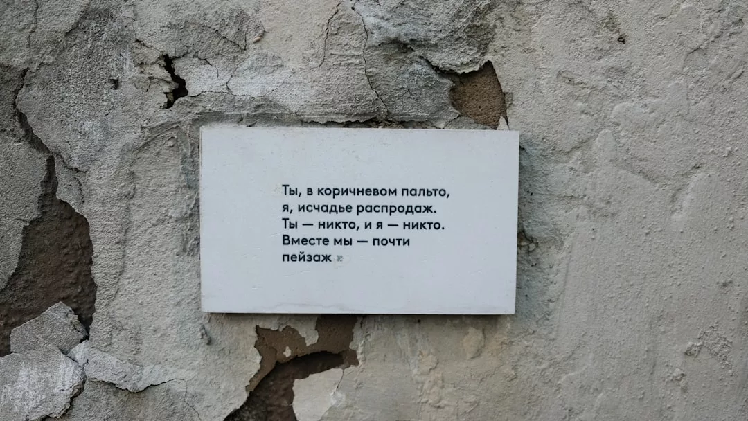 A white plaque with Russian text, possibly a poem or excerpt, is mounted on a cracked, weathered concrete wall—a stark contrast to the luxury lifestyle found in Majorca.