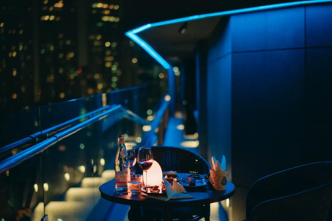 A small table on a balcony at night holds a wine glass, water bottle, and snacks, illuminated by a candle; city lights twinkle in the background, creating a scene of relaxed luxury and lifestyle reminiscent of Majorca evenings.