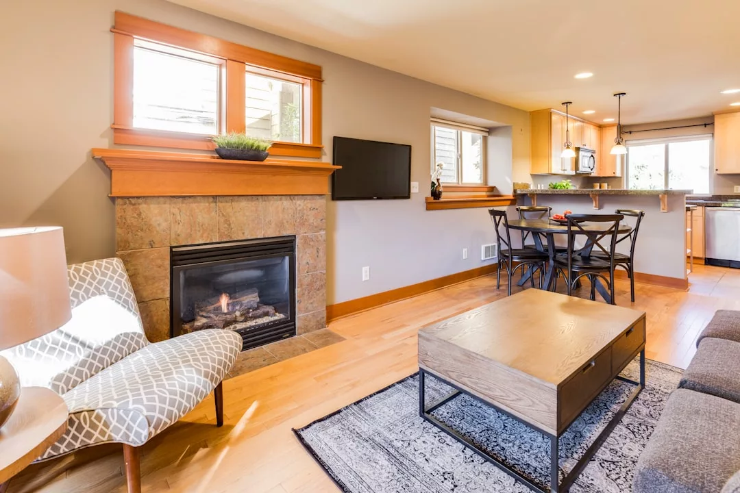 A modern living room exuding luxury, featuring a fireplace, wall-mounted TV, patterned armchair, wooden coffee table, dining area, and an open kitchen in the background—perfect for embracing the relaxed Majorca lifestyle.