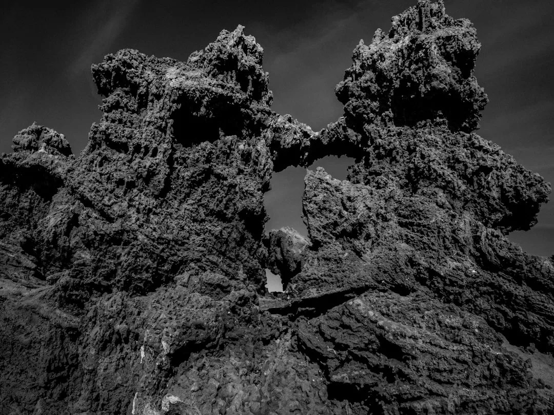 Black and white photo of rugged volcanic rock formations with a natural arch in the center against a cloudy Majorca sky, capturing the essence of island luxury and lifestyle.