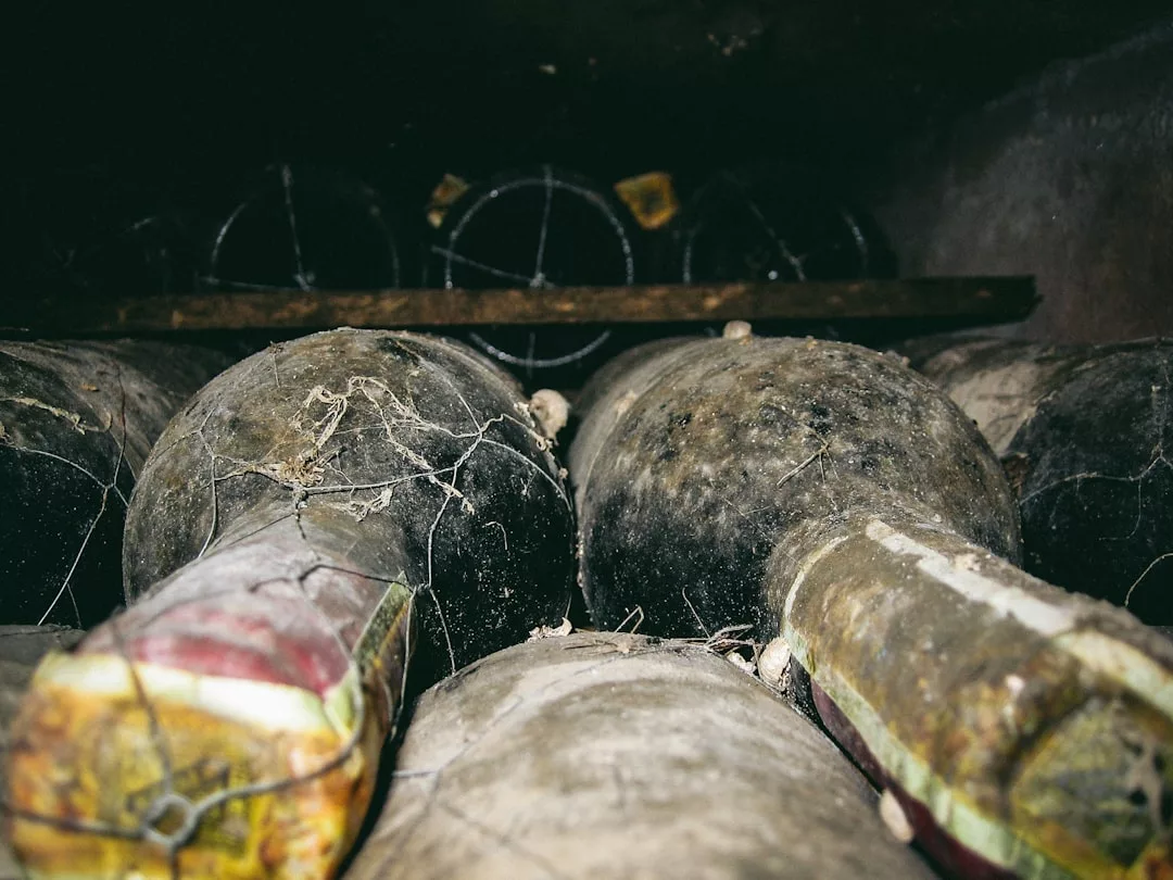 Dusty, cobweb-covered wine bottles are stacked horizontally in a dimly lit cellar, embodying the quiet luxury of a refined lifestyle reminiscent of Majorca’s hidden wine retreats.