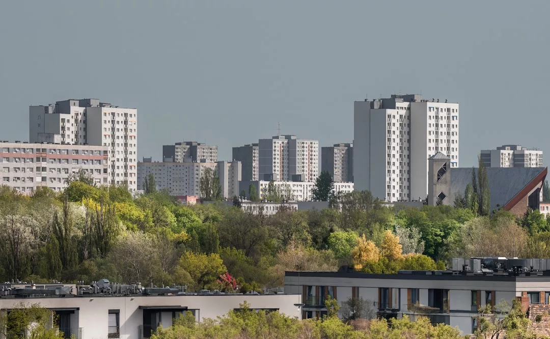 Luxury residential high-rise apartment buildings stand behind a row of trees and low-rise buildings under an overcast sky, offering an elevated lifestyle reminiscent of Majorca.