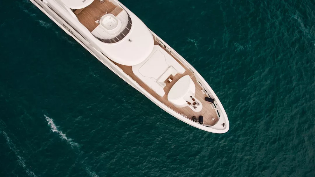 Aerial view of a white luxury yacht cruising on clear, deep blue water off the stunning coast of Majorca.