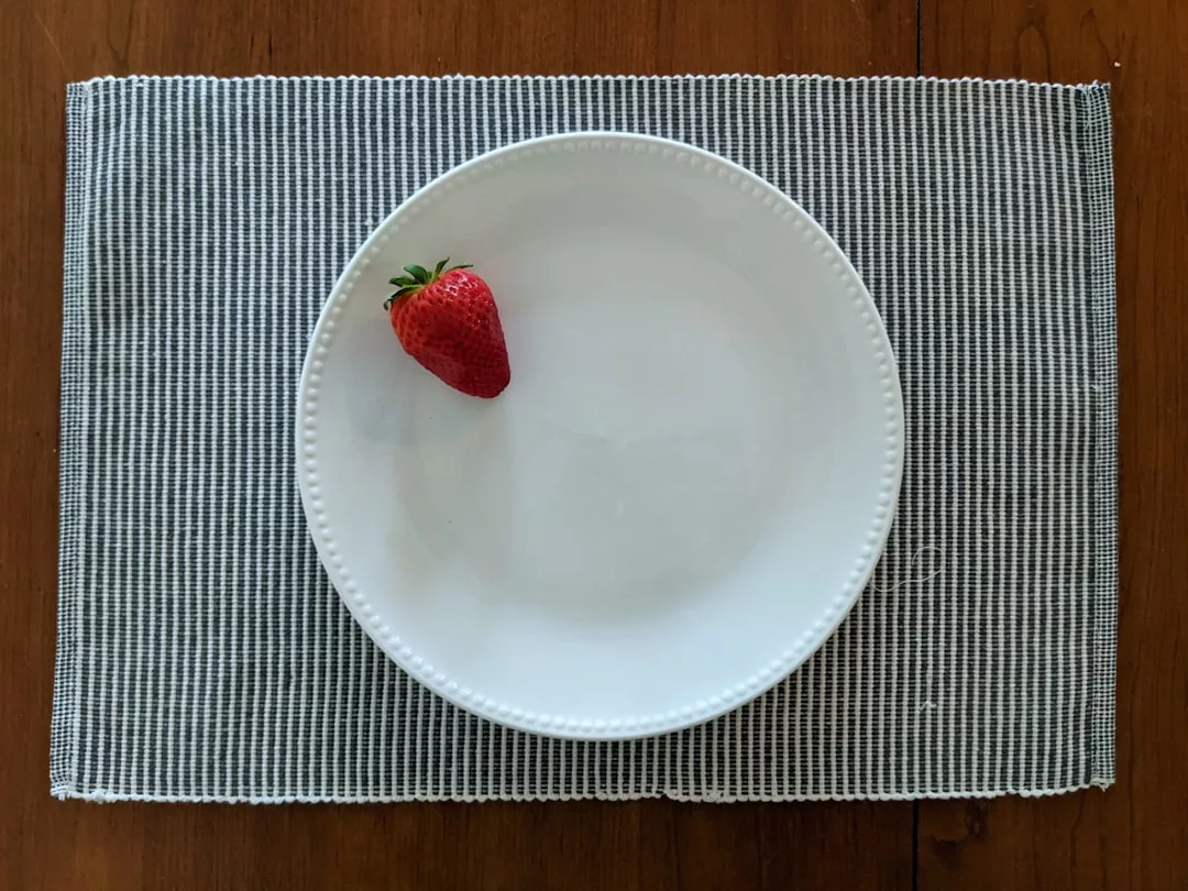 A single strawberry on a white plate, placed on a gray and white woven placemat on a wooden table, evokes the relaxed luxury lifestyle of Majorca.