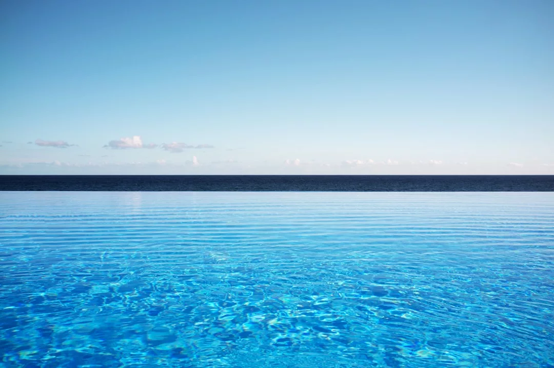 A clear blue infinity pool overlooks a calm ocean under a mostly clear sky with a few scattered clouds, offering the ultimate luxury lifestyle in Majorca.