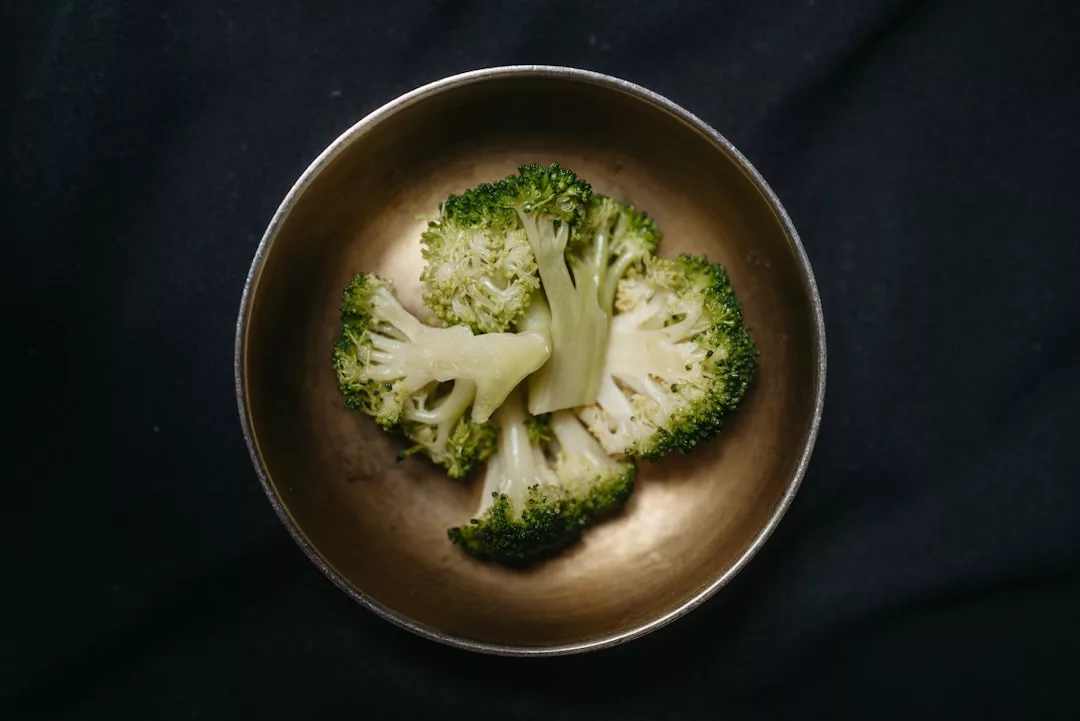 Three pieces of cooked broccoli in a metal bowl evoke a touch of luxury, presented on a dark fabric background.