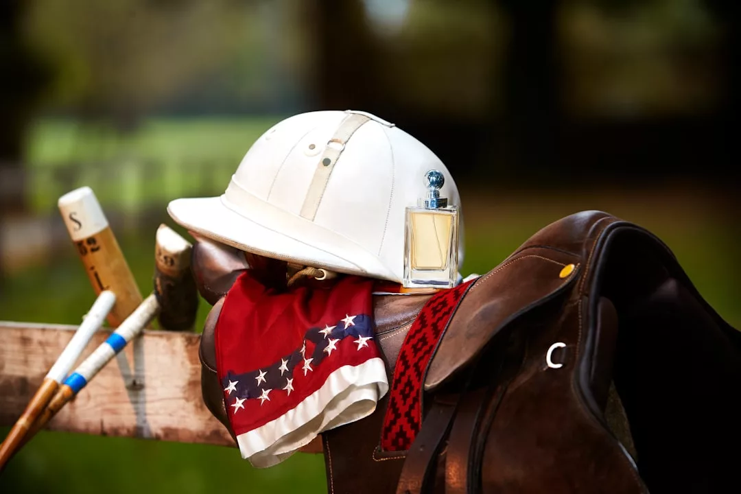 A white polo helmet, red bandana with white stars, and saddle rest on a fence, embodying a luxury lifestyle against a backdrop of polo mallets and the green fields of Majorca.