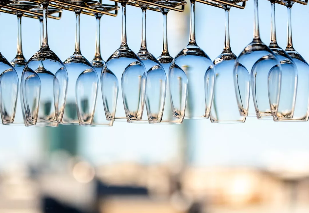 A row of clean wine glasses hang upside down from a rack, reflecting a luxury lifestyle against the blurred outdoor backdrop of Majorca.