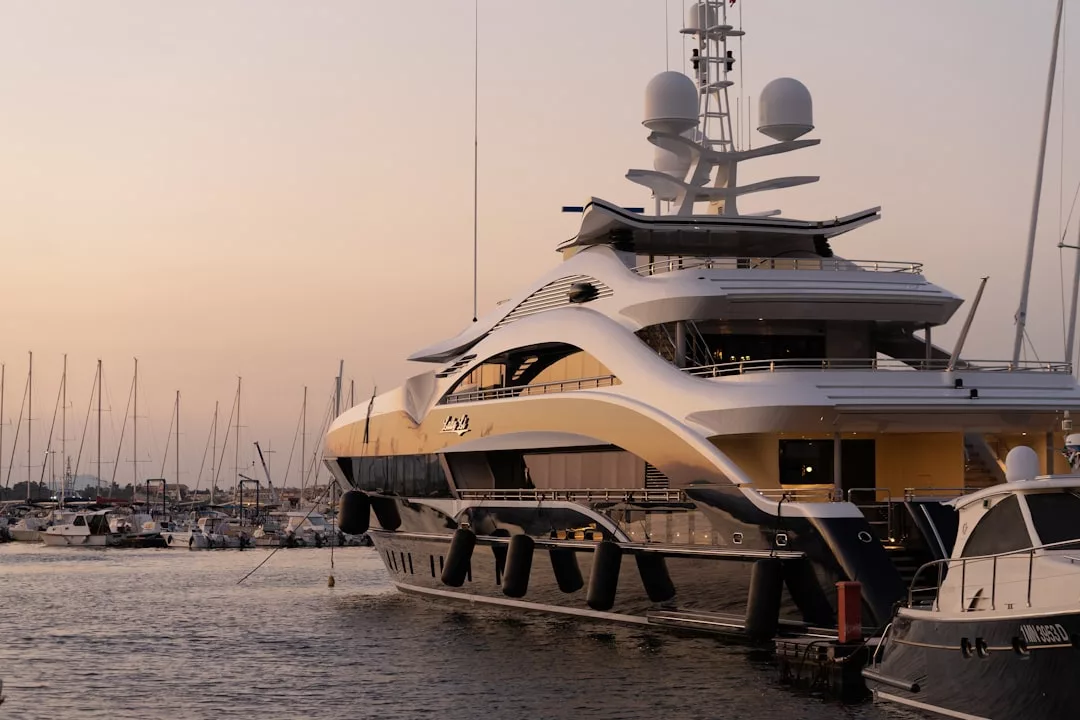 A large luxury yacht docked at a Majorca marina during sunset, with sailboats and masts in the background, captures the essence of an exclusive lifestyle.